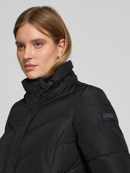 Frauenmodel trägt Steppmantel mit Kapuze von NAUTGÅRD 'NEBULA' in Schwarz, glatte Oberfläche, Detailaufnahme Oberkörper, Regular Fit, verdeckter Reißverschluss, Reißverschlusstaschen, Damen Steppmantel von NAUTGÅRD.