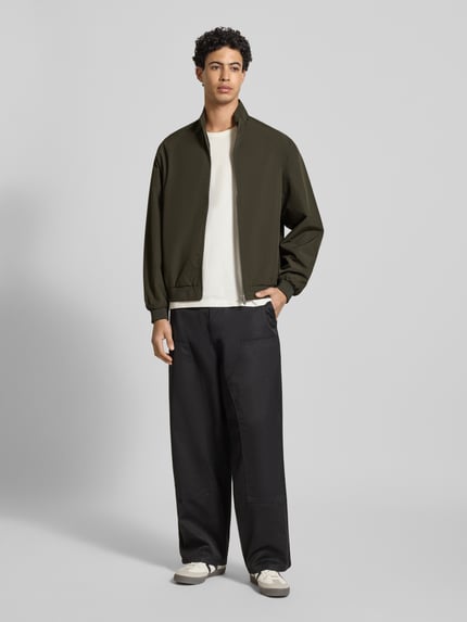 Męski model nosi Regular Fit Jacke mit Stehkragen Modell 'Charge' od Jack & Jones, oliwkowy, gładka tekstura, cała sylwetka z przodu. Długość tyłu w rozmiarze M: 66 cm, szerokość ramion w rozmiarze M: 49 cm, szerokość klatki piersiowej w rozmiarze M: 50 cm, długość rękawa w rozmiarze M: 64 cm.