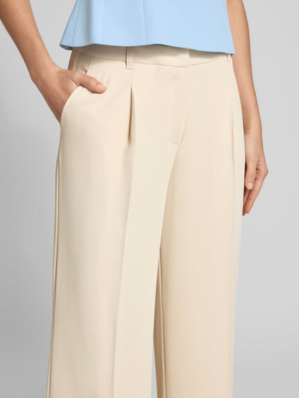 Kobiece modelka nosi Stoffhose mit Bügelfalte von V by Vera Mont w jasnobeżowym kolorze, materiał z domieszką stretchu, krój straight fit, zapięcie na hak i zamek, boczne kieszenie, kant na nogawkach, szerokość w rozmiarze 36: 40 cm, długość nogawki wewnętrznej w rozmiarze 36: 83 cm, detaliczny widok górnej części spodni.