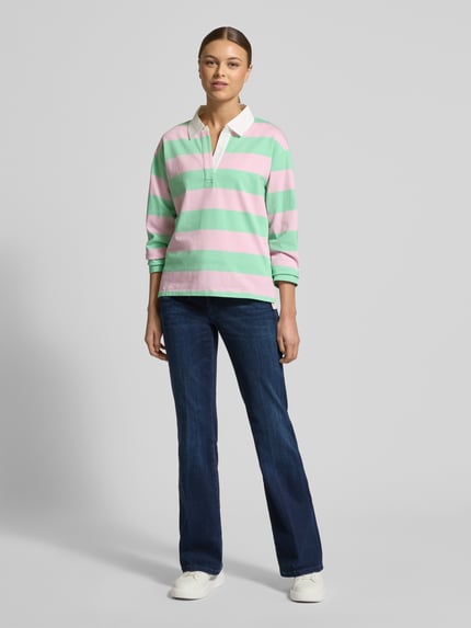 Frauenmodel trägt Regular Fit Poloshirt aus reiner Baumwolle von s.Oliver RED LABEL, gestreift in Rosa und Grün, Piqué-Struktur, Polokragen mit V-Ausschnitt, langarm, Rumpfabschluss mit Seitenschlitzen, ganzkörperansicht von vorne.