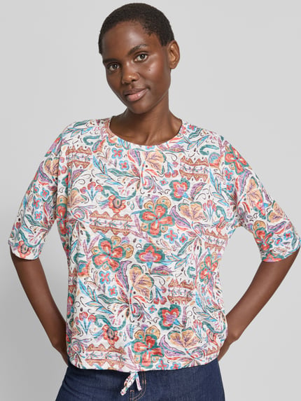 Modelka kobieca ma na sobie T-Shirt im Allover-Look mit 3/4-Arm od Christian Berg Woman, materiał z mieszanką wiskozy, krój regular fit, kolorowy wzór, okrągły dekolt, długość tyłu 52 cm w rozmiarze S, widok całej sylwetki z przodu.