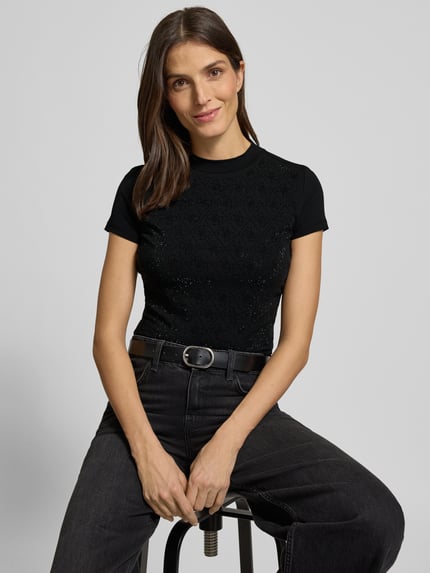 Kobiece model prezentuje Slim Fit T-Shirt mit Allover-Strasssteinbesatz od Guess, czarny, bawełna i elastan, stójka, detal z logo, długość tyłu 51 cm, obszycie z kamieni stras na całej powierzchni, dopasowany krój, zbliżenie na górną część ciała.