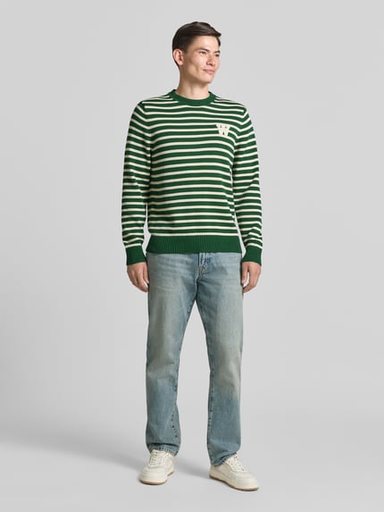 Männermodel trägt Strickpullover mit Rundhalsausschnitt von Wood Wood in Grün-Weiß, Reine Baumwolle, Gerader-Schnitt, Label-Stitching, Ganzkörperansicht von vorne
