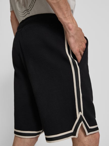 Männermodel trägt Shorts mit Strukturmuster und Label-Stitching von PEGADOR in Schwarz, Baumwolle, Regular-Fit, Eingrifftaschen, Ganzkörperansicht Rückansicht.