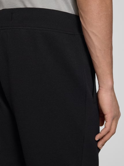Männermodel trägt Straight Fit Shorts mit Strukturmuster von G-Star Raw, dunkles Strukturmuster, Logo-Detail, Nahaufnahme seitlich.