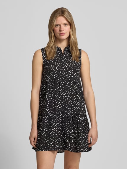 Vrouwenmodel draagt uitlopende dames overhemdjurk van zuivere viscose model 'THEA' van Only met all-over motief, minilengte, zwarte stof met witte stippen, mouwloos design, overhemdkraag, V-hals, plooien, knoopsluiting, rechte zoom, gladde textuur, Ganzkörperansicht von voren.