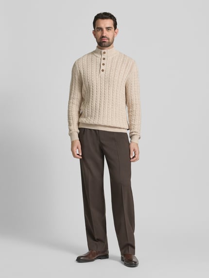 Männermodel trägt Strickpullover mit gerippten Abschlüssen von Fynch-Hatton, Baumwoll-Woll-Mix, Regular-Fit, Stehkragen, Knopfleiste, hellbeige, grobes Zopfmuster, Kombi mit brauner Stoffhose, Ganzkörperansicht von vorne.