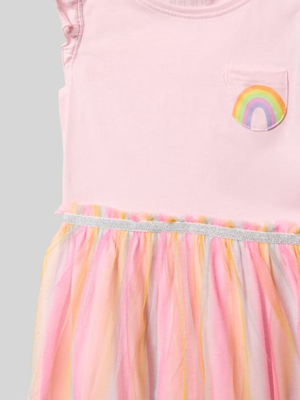 Meisjesmodel draagt 'Kleid mit Brusttasche und Rundhalsausschnitt' van Blue Seven, puur katoen, A-lijn, 2-in-1-look, borstzak, ronde hals, roze met regenboogdetail en veelkleurige tule rok, ruglengte bij maat 116: 23 cm, detailopname bovenlichaam.