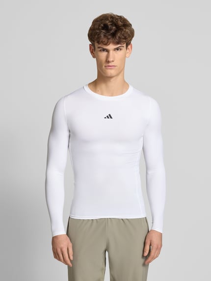 Męski model nosi Longsleeve mit Label-Print od adidas Training, biały materiał z domieszką stretchu, krój slim fit, widok z przodu, ujęcie całej sylwetki.