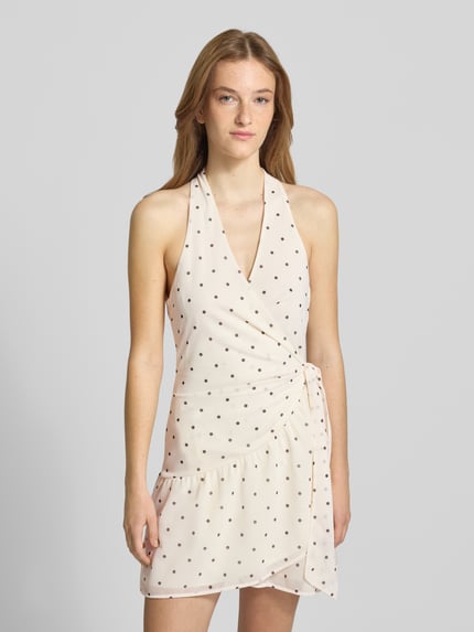 Frauenmodel trägt Minikleid mit Neckholder von Gina Tricot in Wickel-Optik mit Bindegürtel, Taillierte Passform, Creme mit Punkten, Nahaufnahme Oberkörper.