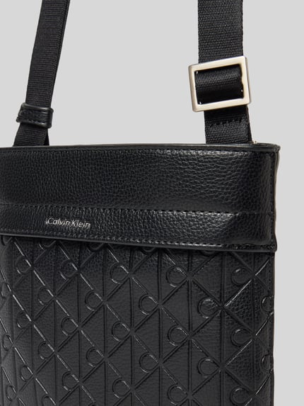Produktfoto, Handtasche mit Label-Detail und Schulterriemen von Calvin Klein für Herren, schwarzer Allover-Look, Struktur, Hauptfach mit Reißverschluss, Breite 21 cm, Länge 19 cm, Tiefe 3 cm, Schulterriemen 73 cm