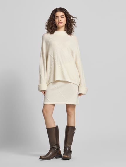 Frauenmodel trägt Regular Fit Pullover mit Alpaka-Anteil Modell 'Liora' von OH APRIL, cremefarben, Strick-Optik, extralange Ärmel, Stehkragen, Ganzkörperansicht von vorne.