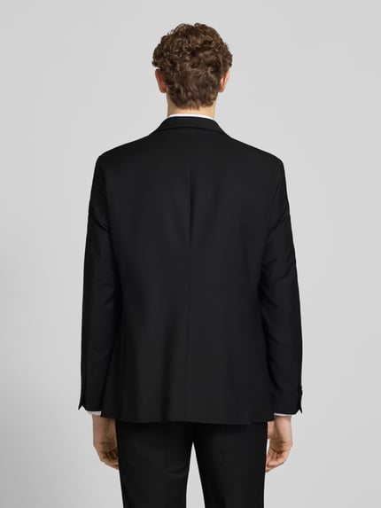 Männermodel trägt Slim Fit Anzug mit 2-Knopf-Sakko Modell 'Grant' von Pierre Cardin, Schwarz, feine Struktur, Ganzkörperansicht Rückansicht.