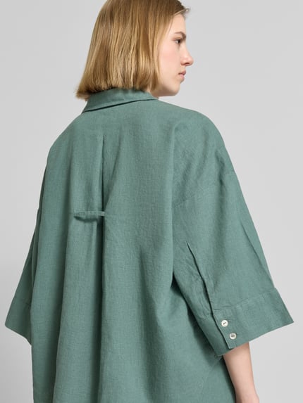 Frauenmodel trägt Boxy Fit Bluse mit V-Ausschnitt Modell 'Lava' von FREE/QUENT aus grünem Leinen-Viskose-Mix, strukturierte Oberfläche, 3/4-Arm, Rückenansicht, Nahaufnahme Oberkörper.
