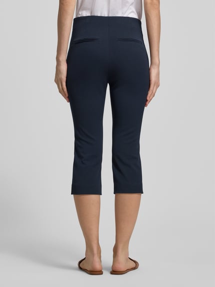 Frauenmodel trägt Caprihose mit Längsnähten von Rich & Royal in Dunkelblau, Slim Fit, Reißverschluss, Gesäßtaschen, Ganzkörperansicht Rückansicht.