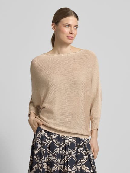 Modelka nosi Strickpullover mit 3/4-Arm od More & More, relaxed fit, okrągły dekolt, długość tyłu 52 cm w rozmiarze 36, długość rękawa 45 cm, beżowy, lekka dzianina, widoczne sploty, gładka tekstura, widok na całą sylwetkę z przodu.