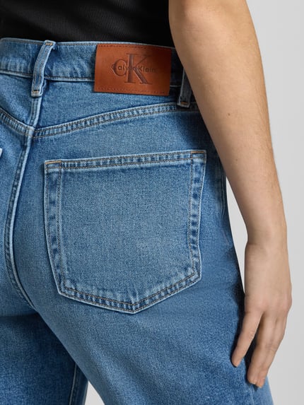 Frauenmodel trägt Straight Fit Jeans mit Logo-Patch Modell 'Mom' von Calvin Klein Jeans, mittelblaue Denimtextur, Detailaufnahme Rückansicht. 5-Pocket-Design, sichtbarer Logo-Patch am Bund, Produktmerkmale laut Kontext.