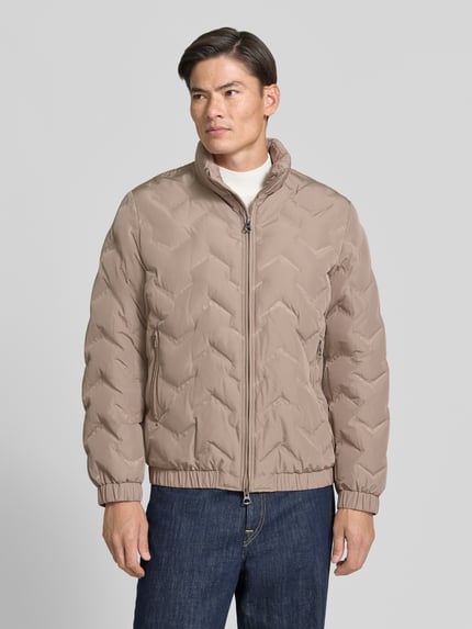 Męski model nosi Steppjacke mit Stehkragen und Reißverschlusstaschen od Antony Morato w kolorze beżowym, krój regular fit, z dwukierunkowym zamkiem oraz bocznymi kieszeniami na zamek, długość tyłu 71 cm, szerokość ramion 50 cm, szerokość w rozmiarze 59 cm, długość rękawa 66 cm, pełny widok z przodu.