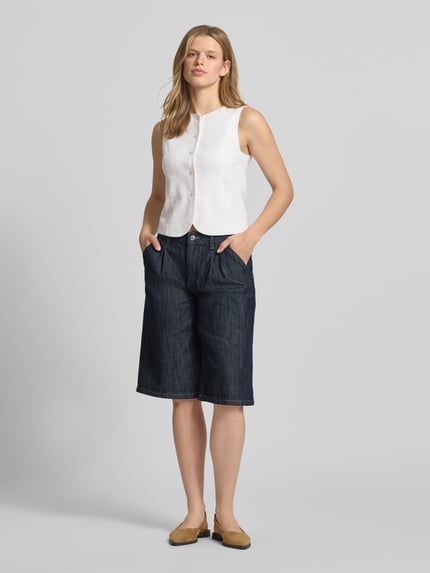 Vrouwenmodel draagt Long Shorts met steekzakken van Gina Tricot in donkerblauw katoenmix met stretch, loose fit, knoop- en ritssluiting, zij- en achterzakken, bandwijdte maat 36: 42 cm, binnenbeenlengte maat 36: 31 cm. Ganzkörperansicht van voren.