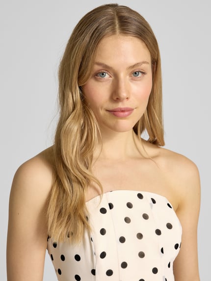 Vrouwenmodel draagt Midikleid im Off-Shoulder-Design Modell 'Kimora' van Forever New, crèmekleurige chiffon met zwarte stippen, a-lijn, detailopname bovenlichaam.