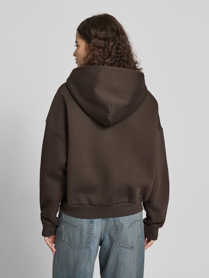 Frauenmodel trägt Sweatjacke mit Logo und Känguru-Tasche von Review in Braun, Relaxed Fit, Baumwoll-Mix, Kapuze, Reißverschluss, Ganzkörperansicht Rückansicht.