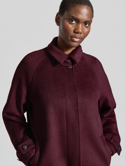 Frauenmodel trägt Regular Fit Mantel mit Stehkragen von Christian Berg Woman Selection in dunklem Bordeaux mit glatter Textur, Nahaufnahme Oberkörper. Rückenlänge 111 cm, Schulterbreite 38 cm, Brustweite 35 cm, Ärmellänge 46 cm, Knopfverschluss und Eingrifftaschen.