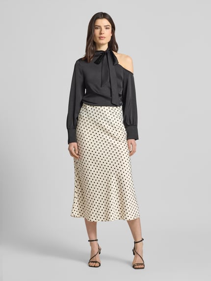 Vrouwenmodel draagt Midirock met zijrits model 'PELLA' van YAS in straight fit, materiaal-mix met stretch, witte stof met zwarte stippen, vooraanzicht volledige lichaamsopname.