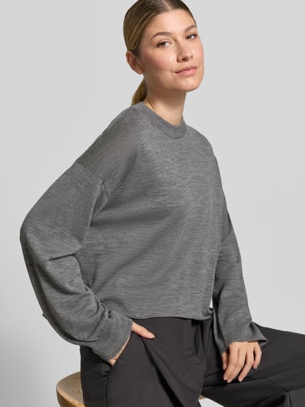 Vrouwenmodel draagt gebreide pullover van zuivere scheerwol in grijs, relaxed fit, ronde hals, Model 'MALESE' van DRYKORN, detailopname bovenlichaam. Ruglengte maat S 49 cm, mouwlengte maat S 52 cm.