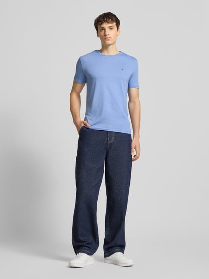 Männermodel trägt Regular Fit T-Shirt aus Baumwoll-Mix von Tommy Jeans in Optik: Unifarben, mit Logo-Stitching, Ganzkörperansicht von vorne.