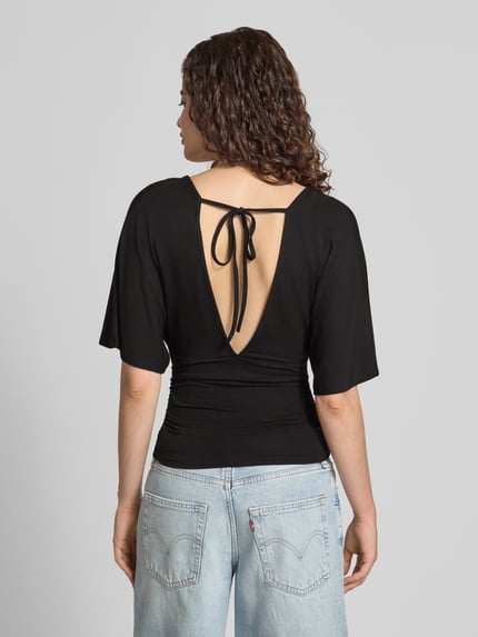 Vrouwenmodel draagt Bluse aus Viskose-Mix mit V-Ausschnitt van Gina Tricot in zwart met getailleerd pasvorm en halflange mouwen, ruglengte maat S 26 cm, mouwlengte maat S 30 cm, viscosemix, rugaanzicht.