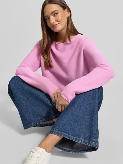 Frauenmodel trägt Strickpullover mit Rundhalsausschnitt und Label-Detail von Fynch-Hatton in Rosa, reine Baumwolle, Regular Fit, kombiniert mit blauen Jeans, glatte Struktur, Ganzkörperansicht von vorne.