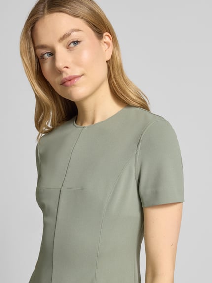 Frauenmodel trägt Knielanges Etuikleid mit Rundhalsausschnitt von Calvin Klein Womenswear, hellgrün, glatte Textur, Nahaufnahme Oberkörper. Material-Mix mit Stretch, gerader Schnitt.