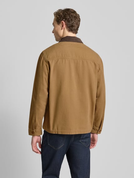 Męski model nosi Hemdjacke mit Kentkragen od Forét z bawełny ekologicznej, krój regular fit, kolor brązowy, wpuszczane kieszenie, długość tyłu 63 cm dla rozmiaru M, widok całej sylwetki z tyłu.