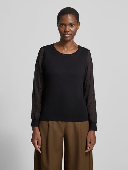 Modelka kobieca nosi Regular Fit Strickpullover aus Viskose-Mix Modell 'Fr44anziska' od ZABAIONE, czarny, z okrągłym dekoltem, rękawy z przezroczystego materiału w kropki, muszelkowe wykończenie, aplikacje z dżetów, długość tyłu w rozmiarze S: 55 cm, długość rękawa w rozmiarze S: 60 cm, krój regular fit, widok całej sylwetki od przodu.