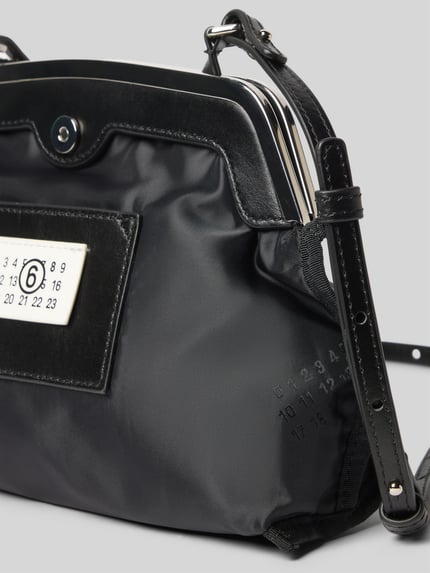 Produktfoto, Saszetka Pochette mit Magnetverschluss von MM6 Maison Margiela, czarny kolor, gładka tekstura, naszywka z logo, nadruk z motywem, główna przegroda, regulowany pasek na ramię, szerokość w rozmiarze 1: 25 cm, długość w rozmiarze 1: 20 cm, głębokość w rozmiarze 1: 9 cm
