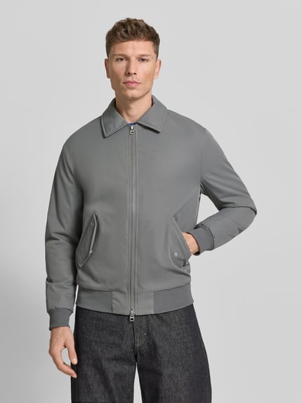 Męski model nosi Jacke mit Reißverschluss od MCNEAL w kolorze szarym, regular fit, kołnierz kent, przód zbliżenie na całą sylwetkę.