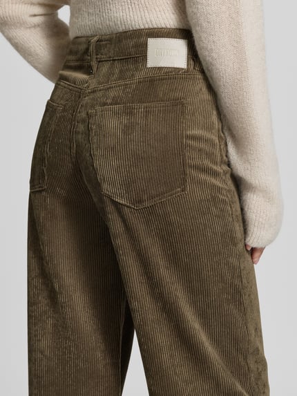 Kobiece modelka nosi spodnie sztruksowe Cordhose mit Eingrifftaschen Modell 'MEDLEY' od DRYKORN w kolorze oliwkowym, krój wide fit, wpuszczane kieszenie, tkanina o prążkowanej fakturze, zapięcie na guzik i zamek błyskawiczny, szerokość w rozmiarze 27/34: 39 cm, długość wewnętrzna nogawki w rozmiarze 27/34: 83 cm, widok na tył, detal.