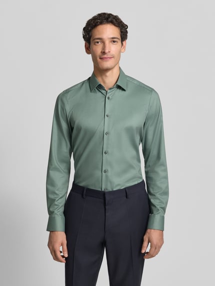 Männermodel trägt Slim Fit Businesshemd mit Kentkragen von OLYMP, unifarben, grüne Webware, langarm, Strukturmuster, Ganzkörperansicht von vorne.