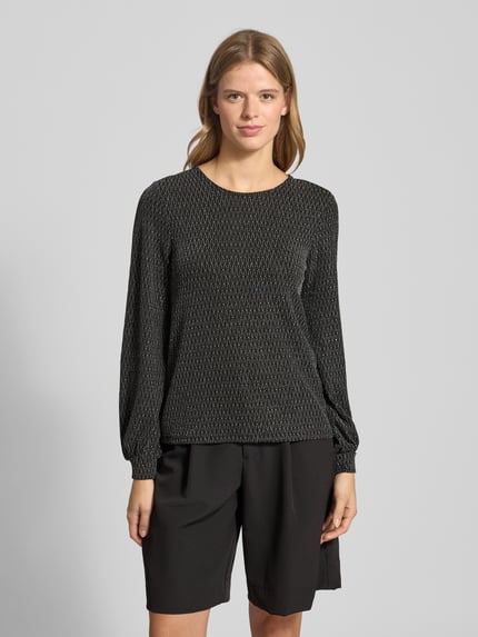 Kobiece modelka nosi Regular Fit Langarmshirt mit auffälligem Metallic Allover-Muster Modell 'CAROL' von Only, czarny błyszczący wzór, długi rękaw, okrągły dekolt, elastyczne wykończenie, perspektiwa: zdjęcie całej sylwetki z przodu.