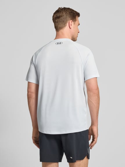 Männermodel trägt T-Shirt mit Label-Print Modell 'Tech' von Under Armour in Hellgrau, Gerader-Schnitt, Rückenlänge 75 cm, Ganzkörperansicht Rückansicht
