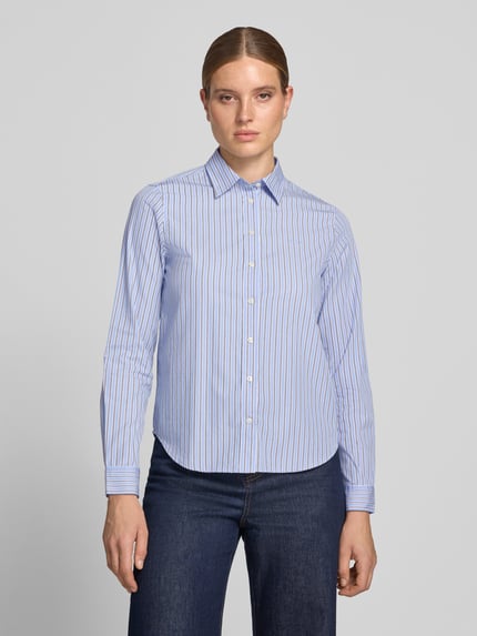 Frauenmodel trägt Regular Fit Langarmbluse aus reiner Baumwolle von GANT, hellblaue und weiße Streifen, glatte Textur, Ganzkörperansicht von vorne.
