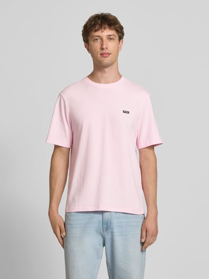 Männermodel trägt T-Shirt mit Label-Patch und Rundhalsausschnitt von REVIEW in Rosa, Reine Baumwolle, Boxy-Fit, Rückenlänge 66 cm, Ganzkörperansicht von vorne.