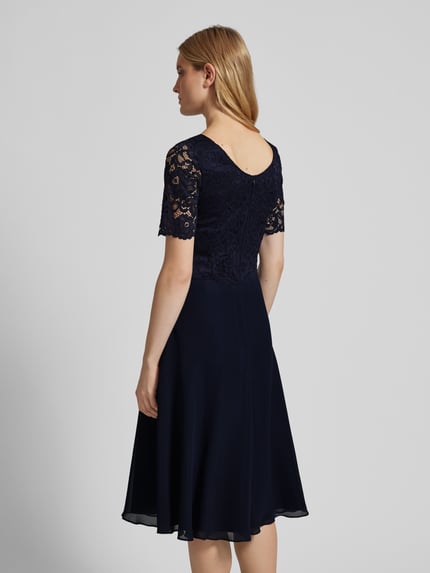 Frauenmodel trägt Cocktailkleid mit Spitzenbesatz von Vera Mont im Unifarbenen-Design aus Material-Mix mit Stretch-Anteil, taillierter Schnitt, Nahtreißverschluss, blickdichtes Unterkleid, Rückenlänge 116 cm, Brustweite 45 cm, Ärmellänge 32 cm, Ganzkörperansicht Rückansicht.