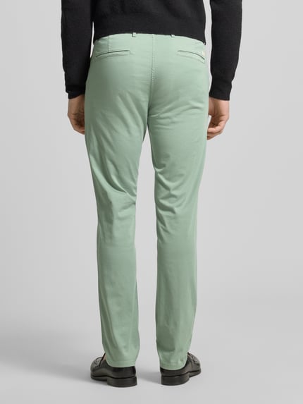 Męski model nosi Slim Fit Chino aus Baumwoll-Mix model 'Chino Slim' von BOSS Orange, efekt: jednolity kolor, krój slim fit, naszywka z logo, szlufki na pasek, zapięcie na guzik i ukryty zamek błyskawiczny, wpuszczane kieszenie z przodu, kieszenie z tyłu, wykończenie materiału: splot twill, materiał: mieszanka bawełny, Ganzkörperansicht Rückansicht.