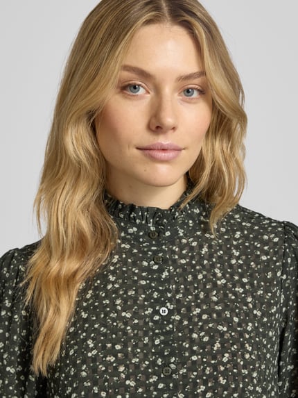 Frauenmodel trägt Relaxed Fit Bluse mit Stehkragen Modell 'Kaylen Oceanna' von MSCH Copenhagen, dunkles Allover-Muster, Nahaufnahme Oberkörper.