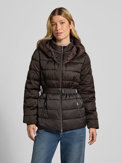 Kobiece model prezentuje Steppjacke mit Reißverschlusstaschen und Gürtel von monari w kolorze ciemny brąz, krój slim fit, kaptur z futerkiem, pasek, dwukierunkowy zamek, kieszenie na zamek, długość tyłu w rozmiarze 36: 67 cm, szerokość ramion w rozmiarze 36: 42 cm, szerokość klatki piersiowej w rozmiarze 36: 49 cm, długość rękawa w rozmiarze 36: 62 cm, widok całej sylwetki z przodu.