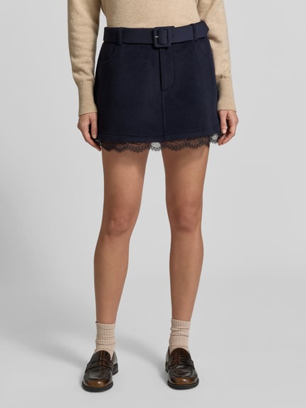 Frauenmodel trägt dunkelblauen Mini-Rock mit Spitzenbesatz von Self-Portrait, unifarben, Schnalle, Gürtelschlaufen, Taschen, Ganzkörperansicht von vorne.