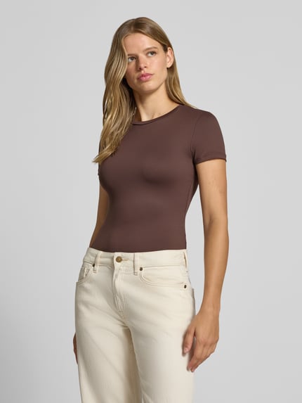 Vrouwenmodel draagt bruin slim fit t-shirt met ronde hals model 'LULA' van PIECES dames, voorkant heupopname.