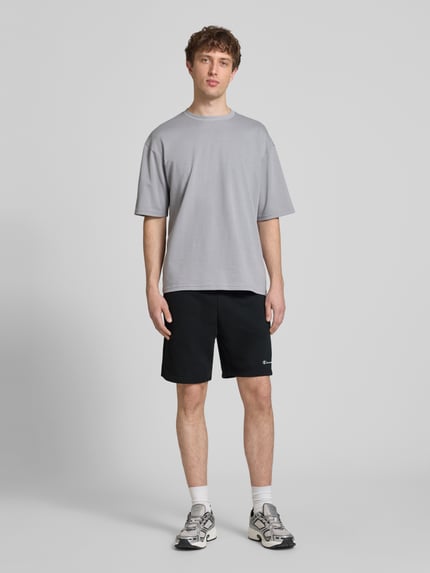 Męski model nosi Shorts mit elastischem Bund und Label-Stitching od CHAMPION, czarny bawełniany miks, krój regular fit, widok całej sylwetki z przodu. Szerokość w rozmiarze M: 43 cm, długość wewnętrzna nogawki: 17 cm.