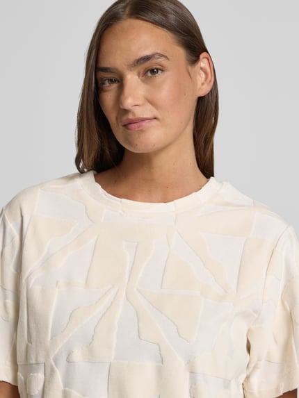 Modelka kobieca nosi T-Shirt im Allover-Look Modell 'NABI' od ICHI z bawełnianej mieszanki, krój regular fit, kremowe, wzór geometryczny, dekolt okrągły, zdjęcie zbliżenie górnej części ciała.